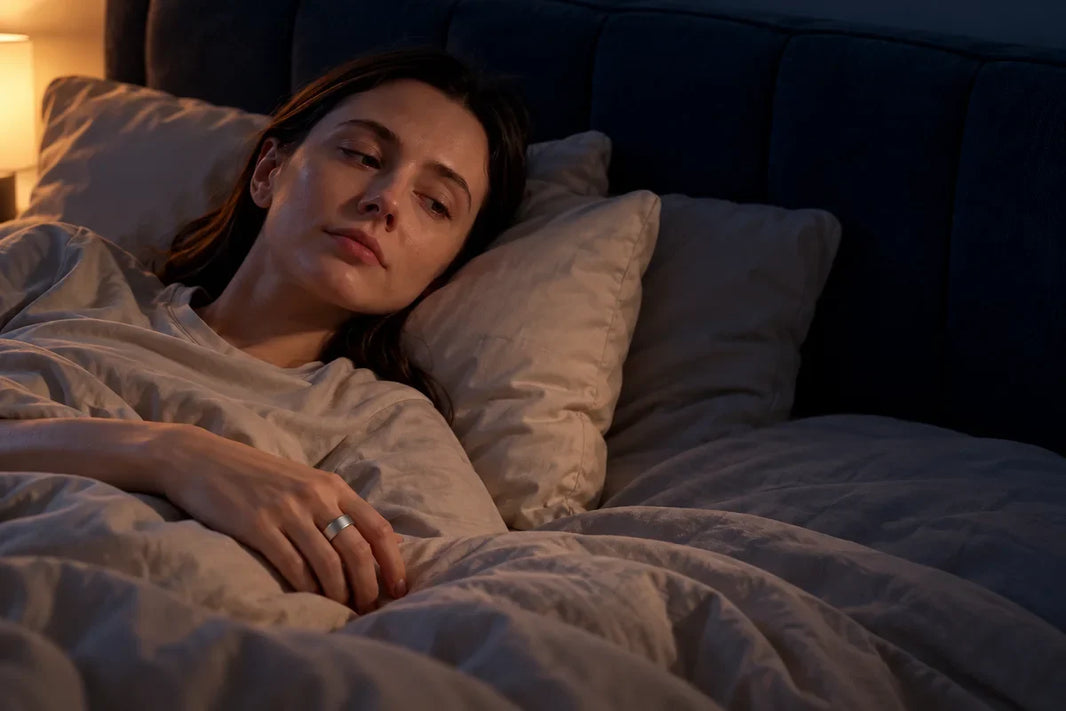 Person awake at night with a silver smart ring on a hand resting on the bed 